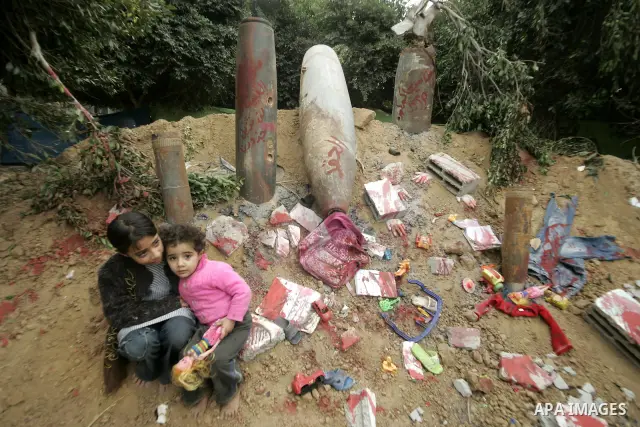 Palestinian children sit near the remains of the ammunition which was used during the war on Gaza at an exhibition organized by Hamas marks the second anniversary of Israel's three-week offensive on Gaza, in the southern...