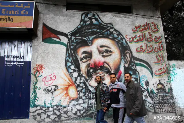 Palestinian men walk in front of a mural of the Palestinian Leader Yasser Arafat, in Gaza City on January 1, 2011. Palestinians celebrating the 46th anniversary of the founding of the Palestinian National Liberation Move...