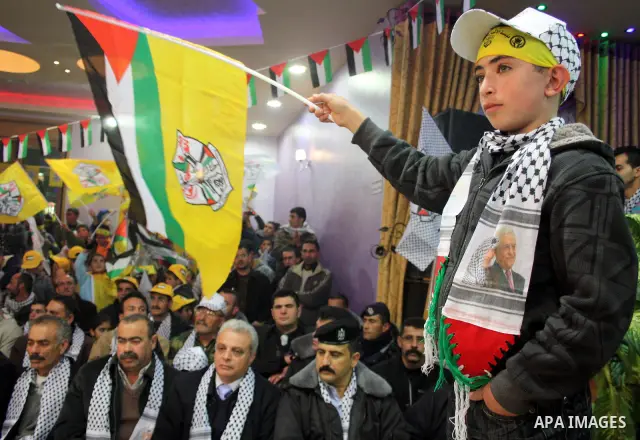 Palestinian supporters of Fatah wave the movement's flag and Palestinian flag during a rally marking the 46th anniversary of the secular party's creation in the village of Halhoul near the West Bank city of Hebron on Jan...