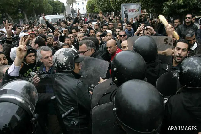 Protestors hold bread as they face riot police officers during a demonstration against the Constitutional Democratic Rally, RCD, party of Ben Ali in the center of Tunis, Tuesday, Jan. 18. 2011. Four ministers quit Tunisi...