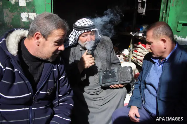 Palestinian men listen to the Radio in front of his shop in the West Bank city of Hebron on 24 January 2011 concerning the 1,600 secret documents published by Al-Jazeera about the Israeli Palestinian negotiations. Palest...