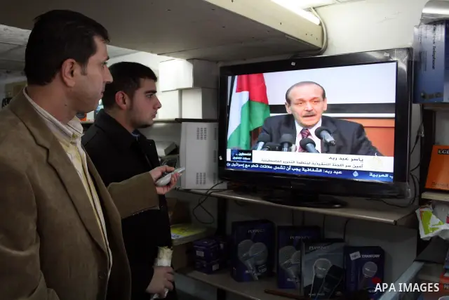 Palestinian men watch TV as a Secretary General of the Council of the Palestine Liberation Organization (PLO), Yasser Abed Rabbo, speaks during a press conference, in the West Bank city of Hebron on 24 January 201 concer...