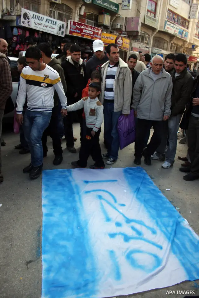 A crowd of Palestinians watches as a fellow protester sprays the name of Al-Jazeera in the place of the Star of David on a make shift Israeli flag before setting it on fire during a demonstration in the West Bank city of...