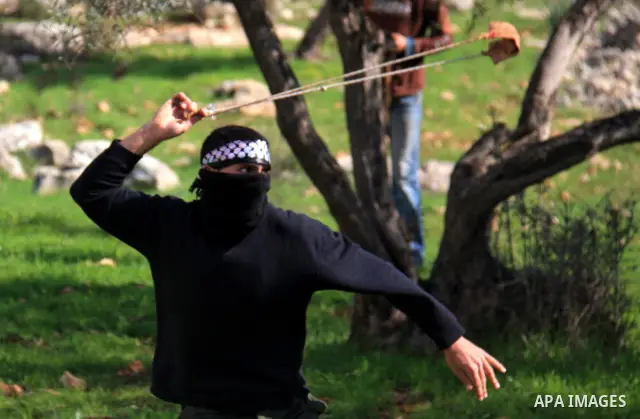 A Palestinian youth uses a sling to hurl stones towards Israeli soldiers during the weekly demonstration against Israel's separation barrier in the West Bank village of Bilin near Ramallah, Friday, Feb. 11, 2011. Photo b...