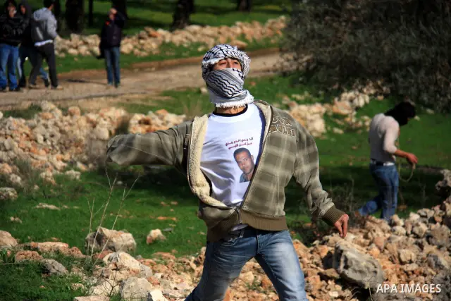 A Palestinian youth hurls stones towards Israeli soldiers during the weekly demonstration against Israel's separation barrier in the West Bank village of Bilin near Ramallah, Friday, Feb. 11, 2011. Photo by Wagdi Eshtaya...