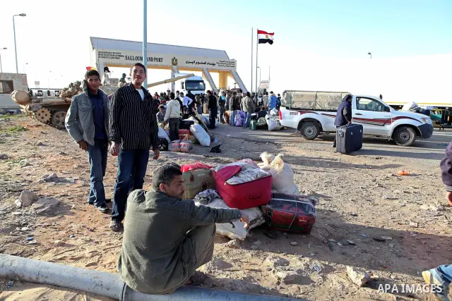 Egyptians, who have fled from Libya through the Salloum land port gate, background, wait with their luggage,Tuesday, Feb. 22, 2011. An estimated 5,000 Egyptians have returned home from Libya by land, and about 10,000 mor...