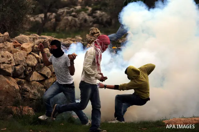 Palestinian youths run for cover from tear gas canisters fired by Israeli soldiers during a protest against the controversial Israeli barrier in the West Bank village of Bilin near Ramallah, Feb. 25, 2011. Photo by Issam...