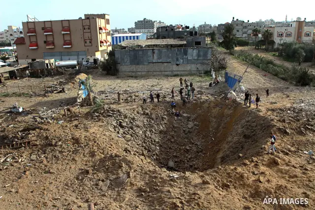 Palestinians stand next to a crater left after a missile fired from an Israeli warplane hit Nusairat refugee camp, Central Gaza strip, Saturday, Feb. 26, 2011. The Israeli airforce attacked Friday night several targets i...