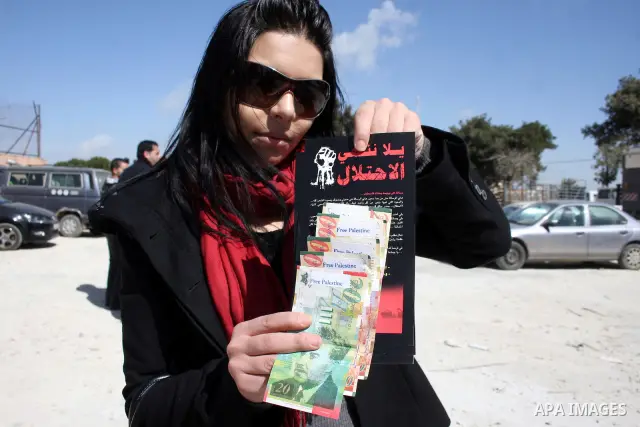 A Palestinian activist holds News Israeli Shekels' bills marked with stickers reading "Free Palestine" on March 7, 2011 in the West Bank city of Ramallah, as part of a campaign aimed to peacefully express opposition to I...