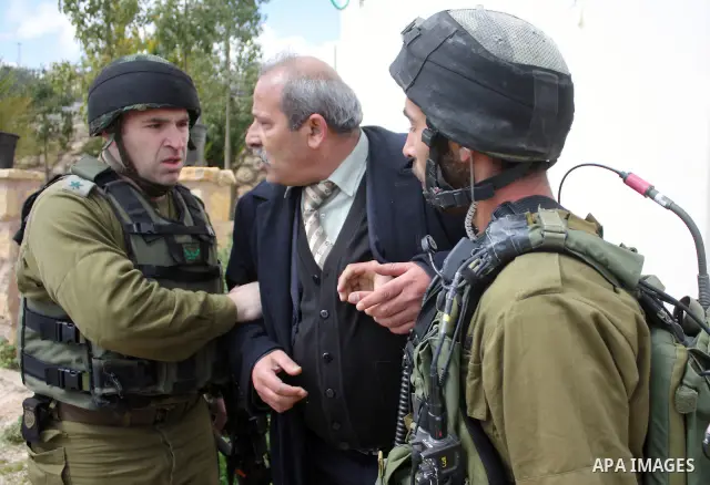 Israeli soldiers arrest a demonstrator as Palestinian men (not seen ) wave their national flag as they sit and block Road 60, which links Jerusalem and Hebron and is used by both Palestinians and Jewish settlers, on Marc...