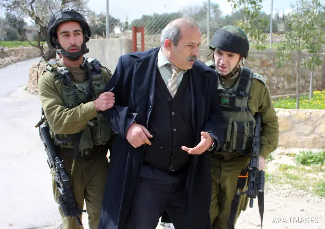 Israeli soldiers arrest a demonstrator as Palestinian men (not seen ) wave their national flag as they sit and block Road 60, which links Jerusalem and Hebron and is used by both Palestinians and Jewish settlers, on Marc...