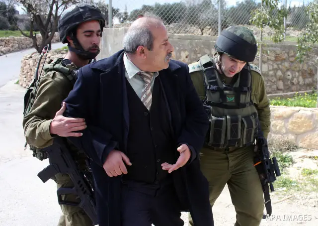 Israeli soldiers arrest a demonstrator as Palestinian men (not seen ) wave their national flag as they sit and block Road 60, which links Jerusalem and Hebron and is used by both Palestinians and Jewish settlers, on Marc...