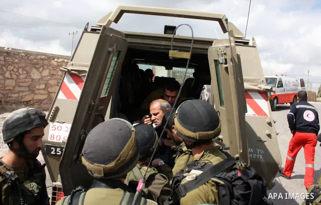Israeli soldiers arrest a demonstrator as Palestinian men (not seen ) wave their national flag as they sit and block Road 60, which links Jerusalem and Hebron and is used by both Palestinians and Jewish settlers, on Marc...
