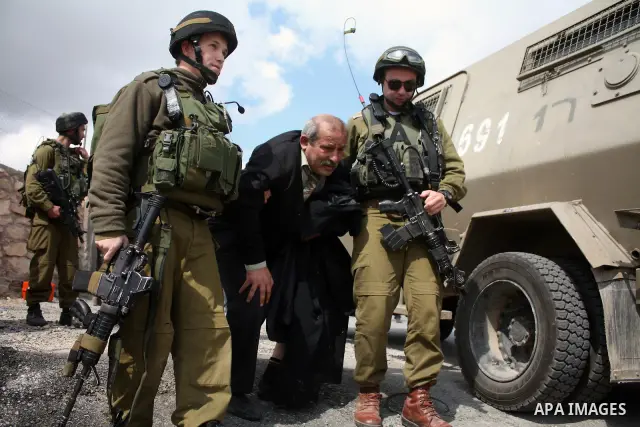 Israeli soldiers arrest a demonstrator as Palestinian men (not seen ) wave their national flag as they sit and block Road 60, which links Jerusalem and Hebron and is used by both Palestinians and Jewish settlers, on Marc...