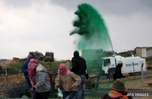 Palestinian protesters run a way as colored water is sprayed by the Israeli army from a water canon during the weekly demonstration against Israel's controversial separation barrier in the village of Bilin, near the West...
