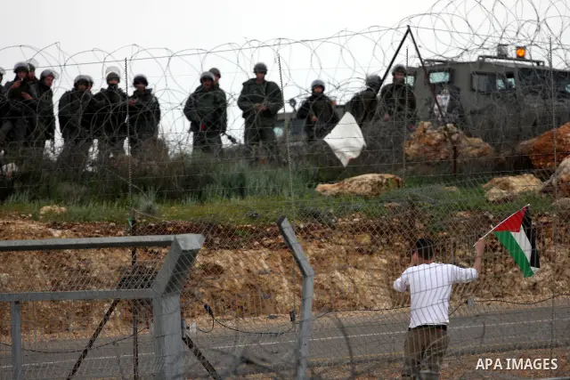 A Palestinian protester waves with national flag in front of Israeli soldiers during the weekly demonstration against Israel's controversial separation barrier in the village of Bilin, near the West Bank city of Ramallah...