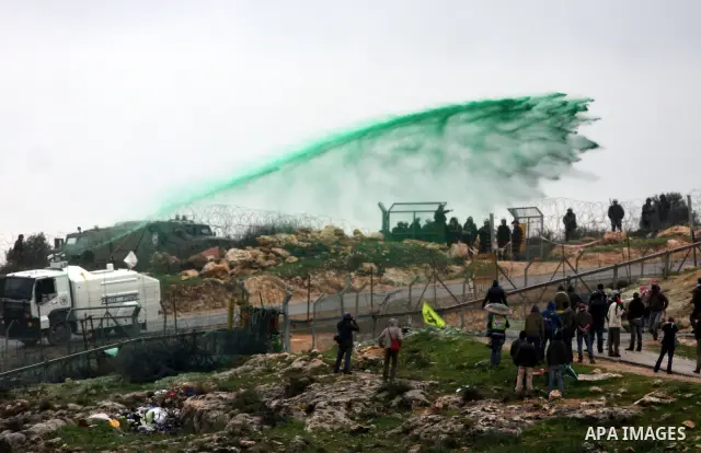 Palestinian protesters run a way as colored water is sprayed by the Israeli army from a water canon during the weekly demonstration against Israel's controversial separation barrier in the village of Bilin, near the West...