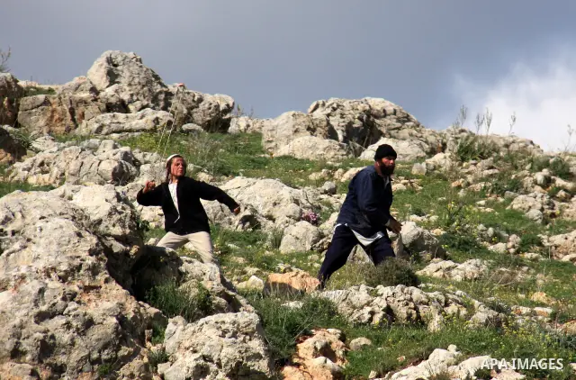 Israeli settlers from the Bracha settlement throw stones at Palestinian youth in the West Bank village of Burin on March 12, 2011 during clashes after an overnight attack in which five members of an Israeli family were k...