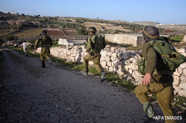 Israeli soldiers stand guard near Israeli settlers from the Kharsina settlement as they prevent settlers from throwing stones at Palestinian cars on March 21,2011 near Hebron in the Israeli-occupied West Bank, as three P...