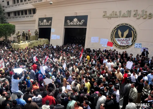 Egyptian police protest in front of the Interior Ministry, calling for a raise in their wages, as army soldiers stand guard atop their armored vehicle in Cairo, Egypt, Tuesday, March 22, 2011. The Arabic on building read...