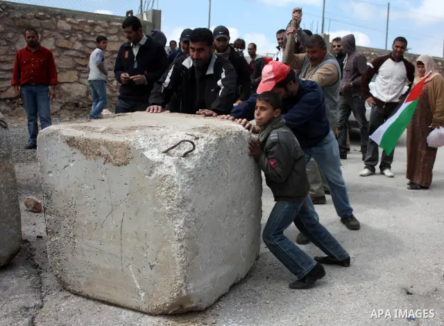 Palestinian, Israeli and foreign peace activists use a metal to move a boulder blocking a road close to a entry point into the Palestinian West Bank village of Beit Omar northen the West Bank city of Hebron on March 26,2...