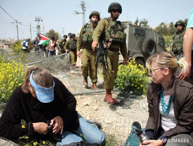Demonstrators sit on a fence during a protest by foreign, Israeli and Palestinian demonstrators against the controversial Israeli separation barrier, in the Palestinian village of Beit Omar, near the West Bank city of He...