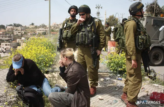 Demonstrators sit on a fence during a protest by foreign, Israeli and Palestinian demonstrators against the controversial Israeli separation barrier, in the Palestinian village of Beit Omar, near the West Bank city of He...
