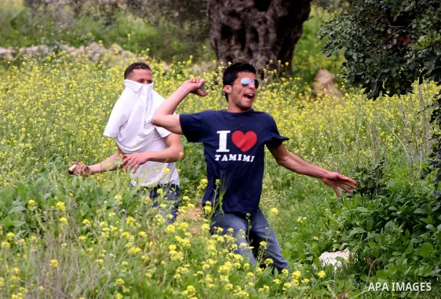 Palestinian youths hurl stones towards Israeli soldiers during a demonstration against the expansion of the nearby Jewish settlement of Halamish in the West Bank village of Nabi Saleh near Ramallah, Saturday, April 2, 20...