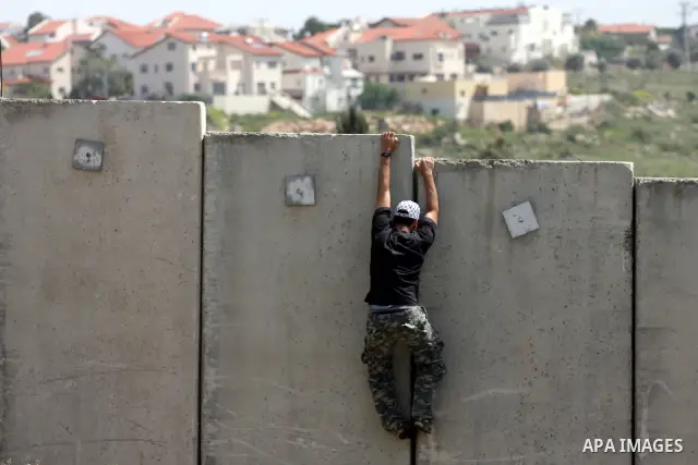 A Palestinian youth climbs the Israeli separation barrier during the weekly demonstration against Israel's separation barrier in the West Bank village of Nilin, near Ramallah, Friday, April 8, 2011. Israel says the barri...