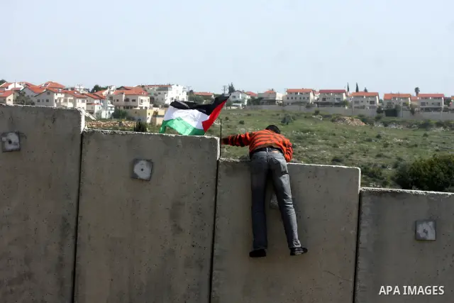 A Palestinian youth climbs the Israeli separation barrier during the weekly demonstration against Israel's separation barrier in the West Bank village of Nilin, near Ramallah, Friday, April 8, 2011. Israel says the barri...