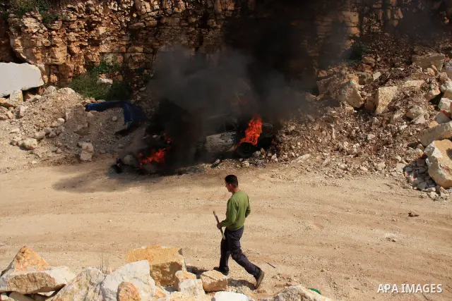 A Palestinian youth walks next to a burning vehicle residents said was torched by Jewish settlers in the West Bank village of Aseera, Saturday, April 9, 2011. Palestinian witnesses said about 40 settlers entered the vill...