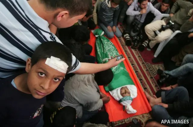 Palestinians sit next to the body of the boy Mahmoud Al-Jaroh who was killed in an Israeli air Strike on Friday, during his funeral at a mosque in Gaza City April 9, 2011. Militant group Hamas said on Saturday it would e...