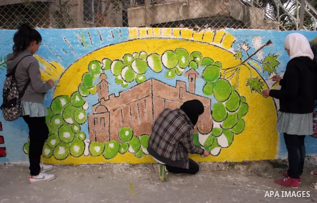 Palestinian students paint on the school wall as a former French football player Lilian Thuram (unseen) looks on during a visit to the divided city of Hebron, in the Israeli-occupied West Bank, on April 13, 2011. Thuram...