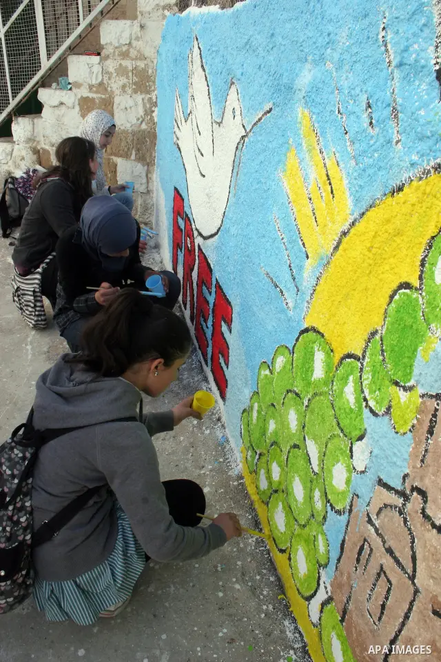 Palestinian students paint on the school wall as a former French football player Lilian Thuram (unseen) looks on during a visit to the divided city of Hebron, in the Israeli-occupied West Bank, on April 13, 2011. Thuram...