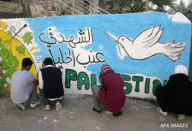Palestinian students paint on the school wall as a former French football player Lilian Thuram (unseen) looks on during a visit to the divided city of Hebron, in the Israeli-occupied West Bank, on April 13, 2011. Thuram...