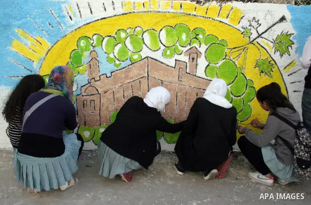 Palestinian students paint on the school wall as a former French football player Lilian Thuram (unseen) looks on during a visit to the divided city of Hebron, in the Israeli-occupied West Bank, on April 13, 2011. Thuram...