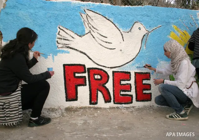 Palestinian students paint on the school wall as a former French football player Lilian Thuram (unseen) looks on during a visit to the divided city of Hebron, in the Israeli-occupied West Bank, on April 13, 2011. Thuram...