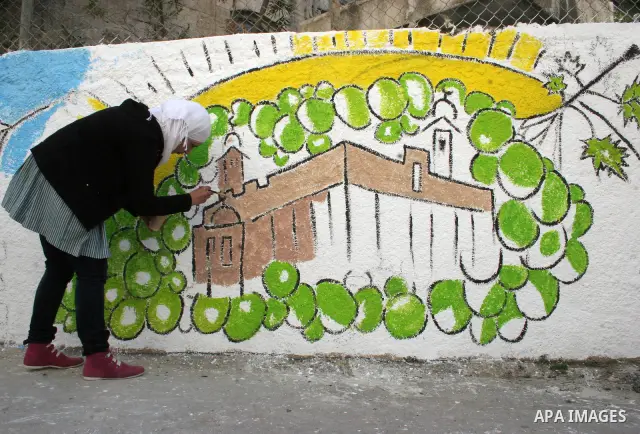 Palestinian students paint on the school wall as a former French football player Lilian Thuram (unseen) looks on during a visit to the divided city of Hebron, in the Israeli-occupied West Bank, on April 13, 2011. Thuram...