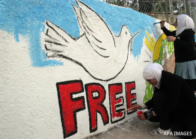 Palestinian students paint on the school wall as a former French football player Lilian Thuram (unseen) looks on during a visit to the divided city of Hebron, in the Israeli-occupied West Bank, on April 13, 2011. Thuram...