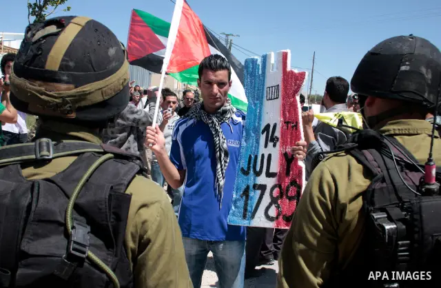 A protester holding a placard depicting the Italian flag and the birth date of Vittorio Arrigoni after kidnapping him in Gaza argue with Israeli soldiers during a demonstration against Israel's controversial separation b...