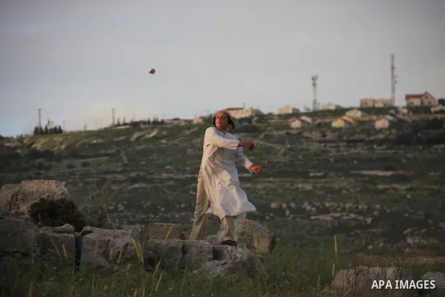 A Jewish settler boy throws rocks at Palestinian protesters, not seen, during clashes over farming land between the Jewish settlement of Bracha and the nearby West Bank village of Burin, near Nablus, Tuesday, April 19, 2...