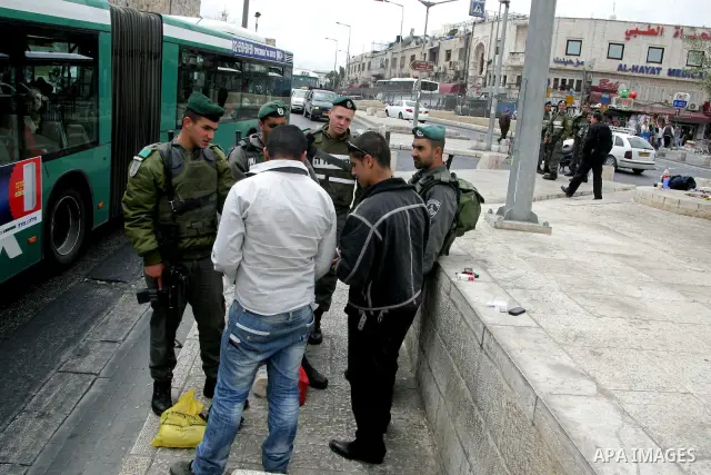 Palestinians walk past an Israeli police officers as they stand guards in the market of the old city of Jerusalem on April 21,2011 photo by MAhfouz Abu Turk