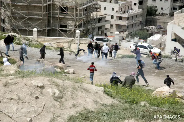 Masked Palestinian youths run for cover from tear gas canisters fired by Israeli soldiers during clashes near a burnt Israeli army vehicle on April 22, 2011 after it flipped over and was set alight by Palestinian youths...
