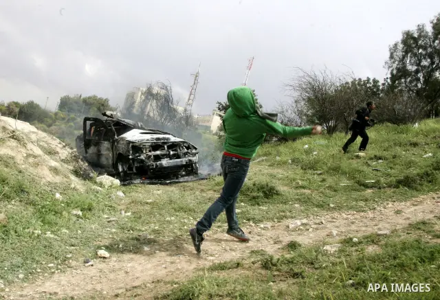 Masked Palestinian youths hurl stones toward Israeli soldiers near a burnt Israeli army vehicle on April 22, 2011 after it flipped over and was set alight by Palestinian youths in the flashpoint neighbourhood of Issawiya...