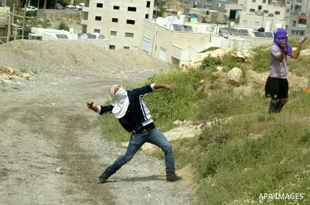 Masked Palestinian youths hurl stones toward Israeli soldiers near a burnt Israeli army vehicle on April 22, 2011 after it flipped over and was set alight by Palestinian youths in the flashpoint neighbourhood of Issawiya...
