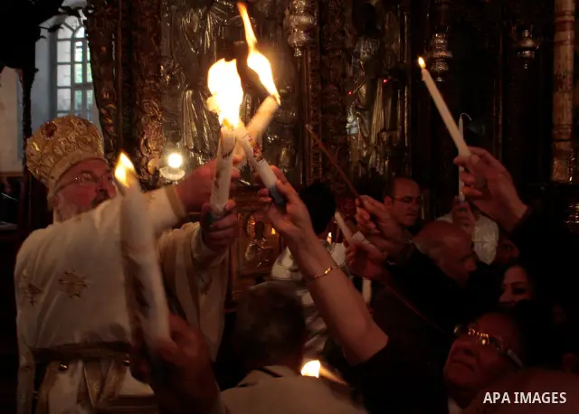 The head of the Greek Orthodox church in Bethlehem Bishop Theofilactos passes the 'Holy Fire' to worshippers brought from the Church of the Holy Sepulchre in Jerusalem during the 'Holy Fire' ceremony on the eve of the Or...