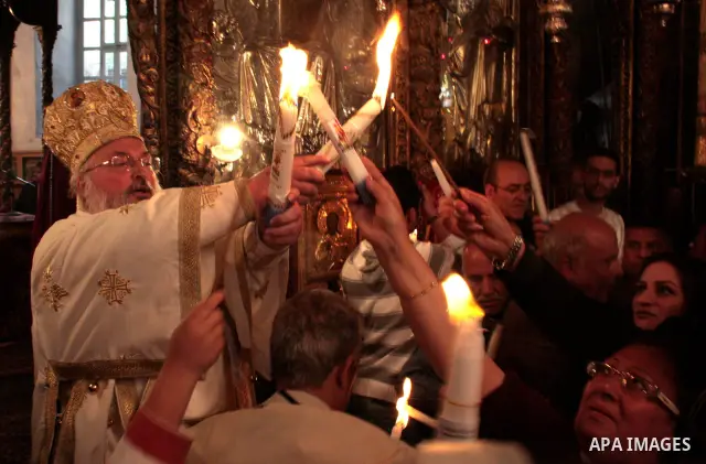 The head of the Greek Orthodox church in Bethlehem Bishop Theofilactos passes the 'Holy Fire' to worshippers brought from the Church of the Holy Sepulchre in Jerusalem during the 'Holy Fire' ceremony on the eve of the Or...