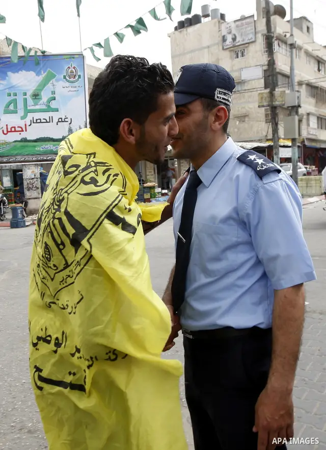 A Palestinian man wrapped with the Fatah party flag shakes hands and kisses a Hamas security man as they celebrate the political reconciliation agreement during a rally in Rafah, southern Gaza Strip, on May 4, 2011 as Pa...