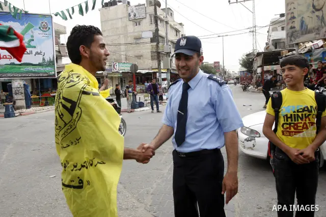 A Palestinian man wrapped with the Fatah party flag shakes hands with a Hamas security man as they celebrate the political reconciliation agreement during a rally in Rafah, southern Gaza Strip, on May 4, 2011 as Palestin...