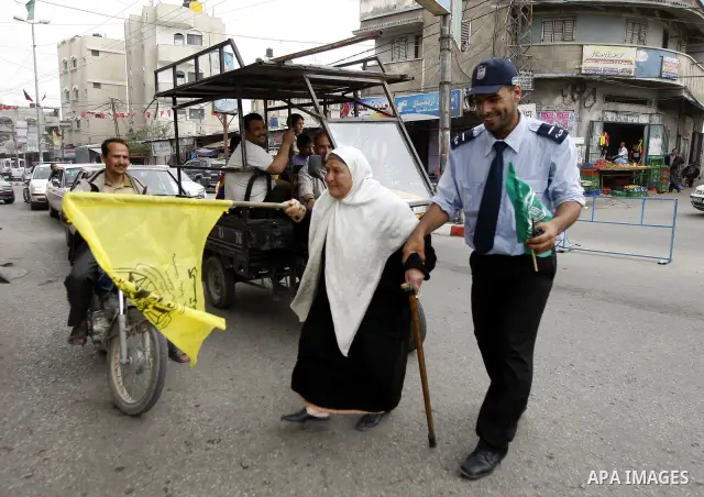 A Palestinian woman waves the Fatah party flag as she is helped to cross the street by a Hamas security man during celebrations to mark the political reconciliation agreement during a rally in Rafah, southern Gaza Strip,...
